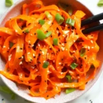 Carrot ribbon salad Asian style topped with sesame seeds and chopped scallions in a bowl