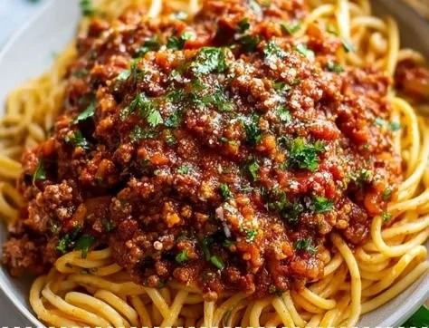 Bowl of homemade meat sauce garnished with herbs, perfect for pasta.